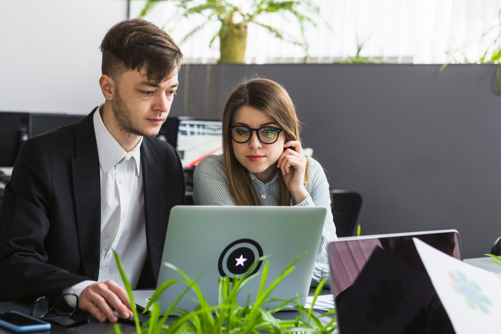 two young businesspeople using laptop workplace scaled